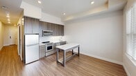 Located at 3444 South Emerson Street in Englewood, Colorado, this one-bedroom, one-bathroom unit offers a well-designed single-level layout that maximizes functionality within a compact footprint. The open-concept living and kitchen area serves as the heart of the unit, featuring warm luxury vinyl plank flooring that flows throughout the space. The kitchen is outfitted with dark wood-grain cabinetry extending to the ceiling for ample storage, stainless steel appliances including a gas range, built-in microwave, refrigerator, and dishwasher, complemented by a clean white countertop island that doubles as a dining surface. Recessed lighting illuminates the space with a bright, modern feel, while crisp white walls and clean-lined trim contribute to a contemporary aesthetic. The bedroom is a comfortable, private retreat with the same warm flooring and neutral wall tones, offering a relaxed and versatile space. The bathroom features a glass-enclosed shower with white subway tile surround and chrome fixtures, maintaining the unit's clean, modern style. A notable convenience is the in-unit stacked Whirlpool washer and dryer, neatly integrated alongside the bathroom. A hallway connects the living areas to the private spaces, rounding out this efficiently planned home.
