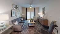 This thoughtfully designed single-floor residence offers a seamless blend of modern style and everyday functionality. The open-concept kitchen serves as a central hub, featuring white shaker cabinetry, granite countertops, a subway tile backsplash, and a large island with bar seating illuminated by Edison-style pendant lights. Black appliances, including a refrigerator, range, and microwave, provide a striking contrast against the bright cabinetry, while wood-look flooring ties the space together.

The living room is generously proportioned, offering a ceiling fan, decorative wall accents, and glass panel doors that introduce natural light and outdoor access. The primary bedroom is carpeted and well-lit with natural light through large windows dressed in dark curtains, complemented by a ceiling fan. A second bedroom features soft carpet, teal patterned drapes, and a dresser, maintaining the home's cohesive aesthetic. A third bedroom presents an elegant upholstered headboard and symmetrical nightstand and lamp pairings.

Two bathrooms serve the residence: one with a walk-in glass-door shower, granite vanity, and wood-look flooring, and a second with a tub-shower combo and built-in shelving. A dedicated in-unit laundry room with a full-size washer and dryer completes this well-equipped home.
