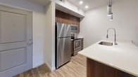This single-floor residence offers a thoughtfully designed open-concept layout that seamlessly connects the main living areas. The kitchen is a standout feature, outfitted with rich walnut-toned cabinetry, stainless steel appliances including a refrigerator, range, and built-in microwave, a classic subway tile backsplash, and a peninsula with a light quartz countertop and undermount sink — ideal for both meal preparation and casual dining. Wood-look luxury vinyl plank flooring runs throughout the kitchen, entryway, hallway, and living area, lending warmth and continuity to the space. The generously sized living room features a ceiling fan, clean white walls, and a glass door that invites natural light and provides access to an outdoor area. A wide hallway connects the living zone to the private quarters, where carpeted bedrooms offer comfort underfoot. At least one bedroom includes a walk-in closet with double rods and shelving, providing ample storage. The bathroom is well-appointed with a walnut-toned vanity, quartz countertop, undermount sink, and a full tub-shower combination with clean white surround panels. Wood-look flooring completes the bathroom's modern aesthetic. Throughout, the space maintains a clean, neutral palette that creates a bright and inviting atmosphere.