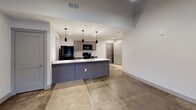 This single-floor space blends modern finishes with industrial character throughout its thoughtfully designed layout. The kitchen serves as a central highlight, showcasing granite countertops, dark taupe cabinetry with brushed nickel hardware, and a full suite of black appliances including a refrigerator, electric range, microwave, and dishwasher. A peninsula with a built-in sink and pendant lighting overhead creates a natural division between the kitchen and the open living area, making it ideal for both cooking and entertaining.

The living area extends from the kitchen and features polished concrete flooring, which carries consistently throughout the unit, adding an urban, loft-like quality to the space. One room demonstrates particularly striking architectural character, with soaring ceilings, exposed wooden beams, painted brick walls, and large windows that invite natural light while maintaining an industrial aesthetic.

The bathroom is clean and functional, finished with granite countertops matching the kitchen, a dark wood vanity, a large mirror, and neutral wall tones. The overall design palette—neutral grays, muted tones, and raw materials—creates a cohesive, contemporary atmosphere with a distinctly modern-industrial edge throughout.
