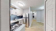Located at 392 State St in North Haven, Connecticut, this single-floor residence has been thoughtfully updated with contemporary finishes throughout. Light wood flooring runs through the main living areas, creating a bright and cohesive aesthetic, while neutral gray tones on the walls lend a clean, modern feel.

The kitchen is a standout space, outfitted with white shaker-style cabinetry accented by matte black hardware, light quartz countertops, and a striking blue subway tile backsplash that adds a bold design element. Stainless steel appliances — including a refrigerator, dishwasher, and range — complete the functional and stylish setup. A hallway connects the kitchen to the rest of the unit, maintaining an open and organized flow.

The living area features wide windows that bring in natural light and offer views of the surrounding greenery, with a wall-mounted HVAC unit ensuring year-round comfort. Bedrooms are carpeted for warmth and comfort, each offering closet storage, including a well-organized built-in shelving unit for additional convenience.

The bathroom is elegantly finished with deep blue subway tile extending floor to ceiling in the tub surround, complemented by grey stone-look floor tile, a modern vanity, and matte black fixtures, tying together the cohesive design language found throughout the home.