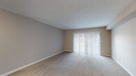 This single-floor unit is thoughtfully laid out to maximize functionality across its living spaces. The living room serves as the central gathering area, finished with neutral-toned carpet and anchored by a large sliding glass door dressed with vertical blinds, allowing an abundance of natural light to fill the room. The textured ceiling and warm beige walls provide a clean, understated backdrop throughout the unit.

From the living area, the flooring transitions to dark hardwood-style planks as you move into the hallway and toward the kitchen. The kitchen features a raised breakfast bar counter and a mosaic tile backsplash, adding a subtle decorative element to the space. A hallway connects the main living area to the bedrooms, each of which is carpeted and painted in neutral tones. The bedrooms receive natural light through window openings fitted with horizontal blinds. Each room also includes closet access, providing practical storage solutions.

The bathroom is finished in crisp white, featuring a full tub-shower combination with tiled surround, a toilet, and a sink. Ceiling vents are present in the bedrooms, indicating a central HVAC system throughout. Overall, the unit presents a clean, functional, and move-in-ready aesthetic.