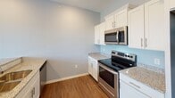 Located along County Road D East in Maplewood, Minnesota, this single-floor unit offers a clean, contemporary design with a cohesive color palette of soft blues and neutral grays carried throughout the space. Wood-style plank flooring runs continuously across the living areas, kitchen, hallway, and bathroom, lending warmth and visual continuity to the interior.

The open-concept layout connects the living area to the kitchen, which is outfitted with white shaker-style cabinetry, granite-look countertops, stainless steel appliances including a range, over-the-range microwave, and refrigerator, and a peninsula with a sink that separates the kitchen from the main living space. Recessed lighting in the kitchen and dining area adds a polished finish.

The living area is generously sized and benefits from abundant natural light through large sliding glass doors that open to a private balcony, offering outdoor views of the surrounding neighborhood. An additional window further brightens the space.

A well-proportioned hallway lined with multiple white panel doors provides access to closets and other rooms, offering notable storage capacity. The bathroom features a full tub-shower combination, a white vanity with granite-look countertops, brushed nickel hardware, and wood-style flooring, maintaining the unit's consistent modern aesthetic throughout.
