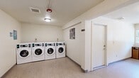 This shared laundry facility at 1066 Sunnyvale Saratoga Rd in Sunnyvale, California, offers a clean, well-organized space designed for efficient, everyday use. The room is laid out in an L-shaped configuration, providing a generous open floor area that comfortably accommodates multiple users at once. The interior features light-colored walls and neutral vinyl flooring, contributing to a bright and tidy atmosphere. Overhead flush-mount lighting ensures the space is well-illuminated throughout. Multiple front-loading and top-loading washers and dryers line the walls, each equipped with digital control panels for ease of use. A built-in folding counter runs along one wall, offering a convenient surface for sorting and folding laundry. A trash receptacle is also provided for user convenience. The facility includes a window that allows natural light to filter in and provides a view of the surrounding greenery. Safety features include a visible fire suppression system and security camera, ensuring a secure and compliant environment. Access is provided through a dedicated entry door. The overall design prioritizes functionality and cleanliness, making this laundry facility a practical and well-maintained amenity for residents.