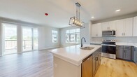 This contemporary townhouse in Elgin, IL, offers 950 square feet of thoughtfully designed living space across two floors. The main floor, comprising 890 square feet, features an open-concept layout that seamlessly blends the kitchen, living, and dining areas. The gourmet kitchen is a standout, boasting white cabinetry, stainless steel appliances, and a large center island with a modern pendant light fixture. Light-toned hardwood floors run throughout the main living areas, creating a bright and airy atmosphere.

The single bedroom, measuring 150 square feet, is generously sized and includes plush carpeting and large windows for natural light. Two well-appointed bathrooms feature contemporary fixtures, including sleek vanities and ample storage. An in-unit laundry room with stacked washer and dryer adds convenience to daily living.

Large windows throughout the home, including sliding glass doors, flood the space with natural light and offer views of the surrounding area. The property's design emphasizes clean lines and a neutral color palette, creating a modern and inviting ambiance. With its efficient use of space and upscale finishes, this townhouse offers comfortable urban living in a desirable location.