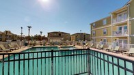 Located at 14510 Lemoyne Blvd in Biloxi, Mississippi, this residential community offers a welcoming Gulf Coast living experience defined by its bright, open surroundings and well-appointed shared amenities. The property's exterior showcases warm yellow stucco-finished multi-story buildings accented with white trim and private balconies, creating a cheerful and cohesive architectural aesthetic that is characteristic of coastal Southern design.

At the heart of the community is a generously sized outdoor swimming pool with clear turquoise water, serving as a central gathering point for residents. The pool deck is outfitted with numerous lounge chairs and seating areas, providing ample space for sunbathing and relaxation beneath the expansive blue sky. A white fence perimeter neatly defines the pool area, while black iron railings along elevated walkways offer safe and scenic vantage points overlooking the amenity space.

Mature palm trees and tasteful landscaping are visible throughout the grounds, enhancing the tropical, resort-like atmosphere of the community. Decorative street-style lamp posts add a charming touch to the outdoor environment. The single-floor unit layout ensures convenient, accessible living, while the overall design and shared outdoor spaces reflect a community built for comfort and enjoyment in the heart of the Mississippi Gulf Coast.