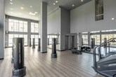 Located at 100 Zoo Lane in Santa Ana, California, this single-floor fitness center offers a generously sized workout space designed to accommodate a wide range of exercise activities. The facility is defined by its striking double-height ceilings, which create an open, airy atmosphere and contribute to a sense of expansive volume throughout the room.

Large, floor-to-ceiling windows line the perimeter, flooding the interior with abundant natural light and providing views of the surrounding outdoor greenery and courtyard. The light-toned hardwood-style flooring complements the soft sage-green walls, giving the space a clean, modern aesthetic.

The main open area is well-equipped with multiple freestanding TKO sparring partner heavy bags, ideal for boxing and martial arts training. A full-length mirror wall runs along one side of the room, enhancing both the functional and visual depth of the space. Recessed lighting supplements the natural light, ensuring consistent illumination throughout the day.

A dedicated cardio zone houses a treadmill and a step mill stair climber, while additional equipment and storage racks are positioned along the walls. The open floor plan allows for flexible use, supporting everything from strength training to group fitness activities. The overall ambiance is bright, welcoming, and purpose-built for an active lifestyle.