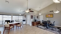 Located at 9350 S Padre Island Dr in Corpus Christi, Texas, this single-floor professional office space combines a welcoming aesthetic with a highly functional layout. The interior is defined by striking vaulted ceilings that lend an airy, open feel throughout, accentuated by stylish pendant lighting and ceiling fans that keep the atmosphere comfortable and well-lit.

The main workspace features multiple workstations with clean, modern white desks paired with warm walnut-toned cabinetry and ergonomic seating. A dedicated conference area anchors one side of the space, centered around a round meeting table surrounded by mesh office chairs, a wall-mounted flat-screen display, and a credenza with a coffee station — ideal for client meetings or team collaboration.

Large windows along the front of the space flood the interior with natural light and provide views of the surrounding outdoor area, enhancing the open, inviting atmosphere. Light wood-look flooring runs throughout, complementing the neutral gray walls and decorative wall art that add a personalized touch. A multifunction printer and additional storage cabinetry support day-to-day operational needs. The front entry features a decorative glass-inset door, creating a polished first impression for visitors.