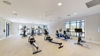 Located at 700 Post Lake Pl in Apopka, Florida, this generously sized fitness center offers a comprehensive, multi-zone layout designed to accommodate a wide range of workout styles and fitness goals. The facility spans a single floor and is organized into several distinct areas, each purpose-built for specific types of training.

The cardio zone features an extensive row of treadmills positioned alongside large, floor-to-ceiling windows that frame lush outdoor views of palm trees and the surrounding community, flooding the space with natural light. Adjacent areas house ellipticals, stair climbers, and rowing machines beneath ceiling fans that enhance airflow and comfort throughout.

The strength training section is equipped with a full array of resistance machines, weight benches, and cable systems, complemented by floor-to-ceiling mirrors that visually expand the space. A well-stocked free weight area includes tiered dumbbell racks, kettlebells, and flat and adjustable benches, with wall-mounted flat-screen televisions providing entertainment.

A dedicated functional training room features hardwood-style flooring, medicine balls, a plyo box, and mirror walls — ideal for dynamic, high-intensity workouts. A separate cycling studio with spin bikes and a large display screen rounds out the facility. Personal lockers, recessed lighting, and clean neutral finishes contribute to a polished, professional atmosphere throughout.