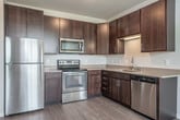 Located at 5355 Nobel Dr in Fitchburg, WI, this one-bedroom, one-bathroom unit offers a well-organized and efficient layout across a single floor. The open-concept living and kitchen area features light hardwood-style flooring, creating a clean and modern aesthetic. The kitchen is equipped with rich dark-wood cabinetry, stainless steel appliances including a refrigerator, range, microwave, and dishwasher, and a functional countertop with a sink — making it a practical and attractive space for everyday living. A hallway connects the main living area to the private quarters, featuring flush ceiling lighting and continued hardwood-style flooring. The bedroom is a cozy, carpeted retreat with neutral tones and a window fitted with blinds that allows natural light to filter in while maintaining privacy. Two closets provide ample storage throughout the unit. The full bathroom includes a dark wood vanity with a single sink and mirror, a tub-shower combination, tile flooring, and chrome fixtures and grab bars, presenting a clean and functional design. The unit's neutral color palette of soft grays and whites throughout creates a bright, cohesive, and move-in-ready atmosphere well-suited for comfortable everyday living.
