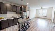 This single-floor unit offers a thoughtfully designed open-concept layout that seamlessly connects the kitchen and living area. The kitchen is well-appointed with dark espresso cabinetry, light stone-toned countertops, and a full suite of stainless steel appliances, including a refrigerator, dishwasher, microwave, and range. Light wood-look flooring runs throughout the main living areas, complementing the neutral wall tones and textured ceilings fitted with recessed lighting.

The open living area extends naturally from the kitchen and is equipped with a ceiling fan, while a large window allows natural light to fill the space with views of the surrounding cityscape. An in-unit laundry closet with a full-size washer and dryer adds practical convenience.

Both bedrooms feature plush carpeting, ceiling fans, and generously sized windows framing urban skyline views. Each bathroom is finished with dark vanity cabinetry, stone-patterned countertops, and wood-look flooring. One bathroom includes a walk-in closet with built-in shelving, while the second offers a spacious vanity with a large mirror. The overall aesthetic is clean, contemporary, and functional throughout.