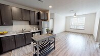 This single-floor unit offers a thoughtfully designed open-concept layout that seamlessly connects the kitchen and living area. The kitchen is well-appointed with dark espresso cabinetry, light stone-toned countertops, and a full suite of stainless steel appliances, including a refrigerator, dishwasher, microwave, and range. Light wood-look flooring runs throughout the main living areas, complementing the neutral wall tones and textured ceilings fitted with recessed lighting.

The open living area extends naturally from the kitchen and is equipped with a ceiling fan, while a large window allows natural light to fill the space with views of the surrounding cityscape. An in-unit laundry closet with a full-size washer and dryer adds practical convenience.

Both bedrooms feature plush carpeting, ceiling fans, and generously sized windows framing urban skyline views. Each bathroom is finished with dark vanity cabinetry, stone-patterned countertops, and wood-look flooring. One bathroom includes a walk-in closet with built-in shelving, while the second offers a spacious vanity with a large mirror. The overall aesthetic is clean, contemporary, and functional throughout.