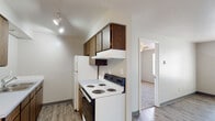 This single-floor unit offers a straightforward, functional layout designed for everyday living. The open living area serves as the main gathering space, featuring wood-style plank flooring, neutral walls, and a panel entry door. A baseboard heating system runs along the perimeter, providing consistent warmth throughout. A ceiling fan with integrated lighting adds air circulation to the space.

The galley-style kitchen is efficiently organized with dark wood cabinetry lining both sides, offering ample upper and lower storage. A double-basin stainless steel sink sits on one side, while a white electric coil range, overhead range hood, and full-size refrigerator are positioned opposite. Track lighting illuminates the cooking area, and wood-style flooring continues underfoot. A doorway connects the kitchen directly to the adjoining room.

A dedicated bedroom features wall-to-wall carpet, a ceiling fan with light fixture, a window that brings in natural light, and a baseboard heater. An electrical panel is mounted on the wall, and a closet door provides convenient storage access.

The bathroom includes a full-size soaking tub and shower combination with white tile surround, a curved shower rod, and a grab bar for added safety. Wood-style flooring and clean white fixtures complete the space.