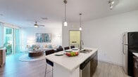 Located at 9301 Summit Centre Way in Maitland, FL, this 1-bedroom, 1-bathroom residence offers a thoughtfully designed, single-floor layout with modern finishes throughout. The open-concept kitchen and living area serves as the heart of the home, featuring a large center island with quartz countertops and bar seating, pendant lighting, and stainless steel appliances including a refrigerator, range, and microwave. White upper cabinetry contrasts with rich dark wood lower cabinets, and wood-style plank flooring runs throughout the main living areas. The living room is bright and airy, with a ceiling fan, large sliding glass door that invites natural light and outdoor views, and ample space for comfortable seating arrangements. A dedicated pantry adds convenient storage to the kitchen area. The bedroom is a serene retreat with plush carpet, a ceiling fan, and a window with exterior views. Three closets provide generous storage throughout the unit. The bathroom features a tiled tub-shower combination, a dark wood vanity with a white countertop, and wood-style flooring. A separate laundry room houses a full-size washer and dryer with overhead shelving, adding everyday convenience to this well-appointed Maitland residence.