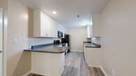 Located at 2205 Woodleaf Rd in Salisbury, NC, this single-floor residence offers a clean, updated interior with a cohesive design carried throughout every room. Durable luxury vinyl plank flooring in a warm wood tone runs continuously across the home, complementing the neutral beige wall palette and bright white trim.

The kitchen is a functional highlight of the space, featuring white shaker-style cabinetry with brushed gold hardware, dark granite-style countertops, and a full suite of black appliances including a range, over-the-range microwave, and refrigerator. A peninsula provides additional prep space, and a secondary sink station with additional cabinetry adds convenience. Textured ceilings are present throughout the home.

The living area is generously proportioned, bathed in natural light from a window overlooking lush greenery, and is equipped with a ceiling fan with integrated lighting. Multiple bedrooms offer comfortable, well-lit spaces, each with windows that bring in natural light and views of the surroundings. Ceiling fans are featured in the bedroom areas as well.

The bathrooms are finished with the same consistent vinyl flooring, clean white fixtures, and open shelving or closet access. Additional closet space is accessible from the bathroom area, adding practical storage. The overall ambiance is bright, clean, and move-in ready.