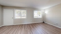 Located at 30 Cattail Ln in North Kingstown, Rhode Island, this two-story home offers a straightforward, well-maintained layout with neutral finishes throughout. The main level features a spacious living area finished with durable wood-look plank flooring and painted in warm neutral tones. Two generously sized windows along the front wall allow ample natural light to fill the room while providing views of the surrounding neighborhood's mature trees. A small built-in cabinet adds a practical detail to the living space.

The kitchen is well-equipped with white cabinetry, dark countertops, and a full suite of white appliances, including a range, dishwasher, and refrigerator. A central island provides additional workspace, and a window above the sink brings in natural light. The main level also includes a half bathroom with wood-look flooring, a white vanity, and a large mirror.

The upper level contains carpeted bedrooms, each with neutral walls, natural light from windows with neighborhood views, and closet storage. A full bathroom on this level features a tub-shower combination, a white vanity, and wood-look flooring. A wood-railed staircase connects both floors, contributing to the home's clean, classic aesthetic.