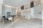 Located at 55 Quebec Ave in Toronto's vibrant west end, this thoughtfully designed single-floor space offers an impressive and versatile layout across two distinct areas. Throughout, light-toned herringbone hardwood flooring lends warmth and visual continuity, while soaring double-height ceilings create a dramatic sense of volume and openness.

The kitchen and dining zone features a sleek, elongated white island with warm wood cabinetry, complemented by a row of modern bar stools. Open shelving, upper cabinetry, and a mezzanine-level glazed clerestory add architectural depth to this area. Floor-to-ceiling sheer drapery diffuses abundant natural light, and recessed ceiling lighting ensures a refined, well-lit atmosphere throughout.

The lounge area exudes a curated, gallery-like ambiance, anchored by a statement area rug in teal and neutral tones. Contemporary seating, a bold large-format artwork, and a sculptural wood coffee table combine to create an inviting yet design-forward environment. Tall sheer curtains frame expansive windows that offer views of the surrounding neighbourhood, further enhancing the bright, airy feel of the space.

Together, the two zones form a cohesive, modern interior well-suited for gatherings, collaborative use, or community amenity purposes.
