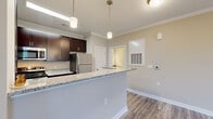 Located at 1006 Cider Mill Loop in Weaverville, NC, this well-designed one-bedroom, one-bathroom residence offers a thoughtful layout across a single floor. The open-concept kitchen and living area serves as the heart of the home, where a peninsula with granite countertops provides both workspace and a natural divide. The kitchen is outfitted with rich dark cabinetry, stainless steel appliances including a refrigerator, range, microwave, and dishwasher, plus tile flooring and pendant lighting that adds a polished touch. Crown molding accents the main living areas, which feature durable wood-style plank flooring and neutral warm-toned walls throughout. The living room is bright and open, complemented by a ceiling fan, while a separate dining area benefits from large windows with blinds that invite natural light. The bedroom is a comfortable retreat with its own closet access and continued wood-style flooring. The bathroom features dark vanity cabinetry with a granite countertop, a tiled tub-shower combination, and tile flooring, completing the cohesive design aesthetic found throughout the residence. Clean white trim and baseboards tie each room together for a fresh, modern feel.