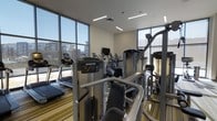 This fitness center is designed to support a comprehensive workout experience within a bright, contemporary setting. The space is characterized by expansive floor-to-ceiling windows along multiple walls, flooding the interior with natural light and offering open views of the surrounding exterior landscape. The modern architectural design incorporates clean lines, recessed linear lighting, and a neutral color palette that creates a clean, energizing atmosphere.

The facility is outfitted with a robust selection of premium Precor-branded equipment, including multiple treadmills, elliptical cross-trainers, and a variety of cable-based strength machines. The equipment is arranged to allow comfortable circulation throughout the space. A wall-mounted television is positioned to be visible from the cardio stations, enhancing the workout experience.

The flooring features a striped, multi-toned carpet that adds a subtle design element while providing a practical surface underfoot. Mirrored wall panels extend the visual depth of the room and allow users to monitor their form during strength training. The overall ambiance is modern, open, and functional, making it a well-appointed facility for a wide range of fitness activities.