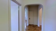 This single-floor space showcases a blend of classic architectural details and functional design. The interior is immediately distinguished by graceful arched doorways that frame transitions between areas, lending the space a refined, timeless character. Underfoot, richly patterned parquet wood flooring adds warmth and visual interest throughout, reflecting the natural light that filters in through well-placed windows.

The neutral, light-toned walls provide a clean and versatile backdrop, complementing the traditional architectural elements and enhancing the overall sense of brightness. The arched entryways create a sense of depth and flow, guiding movement naturally from one area to the next while maintaining an open, connected feel.

White trim and baseboards provide crisp contrast against the warm wood flooring and soft wall tones, reinforcing the cohesive, classic aesthetic found throughout. The layout is organized and efficient, with clearly defined spaces accessible through the distinctive arched corridors. A door with a traditional latch detail adds to the period-appropriate charm of the interior.

Overall, this space offers a well-preserved, character-rich environment defined by elegant architectural touches, warm natural materials, and a bright, airy ambiance that makes it both welcoming and functional.