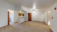This single-floor residence offers a practical and comfortable layout designed for everyday living. The open-concept living area is generously sized, featuring neutral-toned wall-to-wall carpeting, white walls with warm wood trim, a ceiling fan with light fixture, and a baseboard heating system. The space flows seamlessly into the kitchen, which is separated by a peninsula-style breakfast bar — ideal for casual dining or food prep. The kitchen is equipped with warm oak cabinetry, light countertops, a double-basin stainless steel sink, a dishwasher, refrigerator, and a black microwave above the range, all set on light hardwood-style flooring. A sliding glass door in the living area opens to a private balcony overlooking a green outdoor setting, bringing in natural light. The bedrooms are carpeted and well-proportioned, each featuring wood-trimmed doors and closet storage — one with a mirrored sliding-door closet and another with a walk-in style closet. The full bathroom includes an oak vanity with a single sink, a mirror, tile flooring, and a combined tub and shower unit with chrome fixtures. Baseboard heaters are present throughout, and a wall-mounted air conditioning unit provides additional climate control.