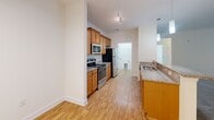 Located at 4301 Cox Pl in Greensboro, NC, this single-floor unit offers a well-organized layout with a neutral color palette and a mix of carpet and hard-surface flooring throughout. The open-concept living and dining area is spacious and bright, featuring plush carpet, a ceiling-mounted light fixture, and a window that allows natural light to fill the space. A ceiling fan with integrated lighting serves one of the carpeted rooms, which also benefits from an outdoor-facing window.

The kitchen is thoughtfully designed with warm honey-toned cabinetry, granite-style countertops, and a peninsula that doubles as a breakfast bar with seating. Black appliances, including a refrigerator, range, and built-in microwave, provide a cohesive look. Light wood-style flooring runs throughout the kitchen, complementing the cabinetry. A pendant lantern fixture above the peninsula adds a decorative touch.

The bathroom features a clean, all-white soaking tub and shower combination with tile surround and light tile flooring. A dedicated laundry room includes washer and dryer hookups, wire shelving for storage, and wood-style flooring. Additional carpeted rooms offer versatile space with crisp white walls and ample room to configure as needed.