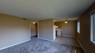 This single-floor residence offers a practical and comfortable layout designed for everyday living. The main living area is finished with plush carpeting and neutral-toned walls, creating a warm and inviting atmosphere. A ceiling fan overhead provides both light and airflow, contributing to the overall comfort of the space.

The living area flows naturally into the kitchen, which transitions to tile flooring and features warm wooden cabinetry that provides ample storage. The kitchen is equipped with a white dishwasher and range, and under-cabinet lighting adds a functional touch. A partial wall separates the kitchen from the living area, maintaining an open feel while subtly defining each zone.

A hallway visible from the main living space leads to additional rooms, suggesting a well-organized floor plan that keeps private and communal areas distinctly separated. The consistent neutral color palette throughout the space lends a cohesive and clean aesthetic. White baseboards and trim provide a crisp contrast against the warm wall tones. Ceiling-mounted vents indicate a central HVAC system for year-round climate control. Overall, the space is straightforward, functional, and move-in ready, offering a solid foundation for comfortable single-floor living.