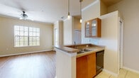 Located at 1930 Devonwood Dr. in Wesley Chapel, FL, this single-floor, one-bedroom, one-bathroom home offers a well-designed layout that maximizes its comfortable footprint. The open-concept living and kitchen area serves as the heart of the home, featuring warm wood-look laminate flooring, crown molding, and a ceiling fan with light fixture. Large windows with blinds invite an abundance of natural light, creating a bright and airy atmosphere. A sliding glass door provides additional light and outdoor access from the living area.

The kitchen is thoughtfully designed with warm wood cabinetry, a breakfast bar peninsula with pendant lighting, tile flooring, and black appliances including a refrigerator, range, and microwave — all framed by a convenient entry foyer just inside the front door.

The bedroom offers plush carpeting, a ceiling fan, and a generously sized window that continues the home's theme of natural light. A dedicated closet provides practical storage. The bathroom features a full tub-shower combination with white tile surround, tile flooring, and clean, neutral finishes. Crown molding and consistent warm-toned walls carry throughout, lending a cohesive and polished feel to the entire space.