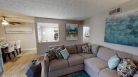 This single-floor residence offers a thoughtfully designed layout that balances comfort and functionality throughout. The entryway welcomes visitors with neutral-toned walls, textured ceilings, and warm hardwood-style flooring that carries through the main living areas.

The living room serves as the heart of the home, featuring a generous open layout with room for a large sectional sofa and complementary furnishings. A pass-through window connects the living area directly to the kitchen, creating an open, communicative flow between the two spaces.

The kitchen is well-equipped with white cabinetry, granite-style countertops, a grey tile backsplash, black appliances including a full-size refrigerator and range, and hardwood-style flooring. Pendant lighting and ample cabinet storage add both style and practicality.

The bedrooms are carpeted and comfortable, each featuring neutral walls and windows that allow natural light to filter in. The primary bedroom includes a walk-in closet with built-in shelving and hanging rods, offering excellent storage capacity.

The bathroom features a full tub and shower combination with tiled surround, hardwood-style flooring, and a vanity with stone-look countertops. Throughout the residence, a cohesive neutral color palette is accented by teal and warm tones, contributing to a calm and welcoming ambiance.