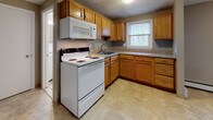 This single-floor unit offers a practical and comfortable layout designed to maximize everyday functionality. The living room is generously proportioned, featuring neutral-toned carpet, warm taupe walls, and white baseboard trim, with multiple windows that invite natural light and offer views of surrounding greenery. Baseboard heating runs along the perimeter, and a wall-mounted air conditioning unit provides year-round climate control.

The kitchen is well-equipped with warm wood cabinetry, granite-look countertops, and a full suite of white appliances, including an electric range, built-in microwave, and a sink positioned beneath a window overlooking the outdoors. The adjacent dining area shares the same tile-style flooring and features additional windows that enhance brightness.

The bedroom is spacious, finished with the same plush carpeting found throughout, a closet, and windows that continue the theme of natural light. The bathroom is clean and simply appointed, featuring a full soaking tub with tiled surround, chrome fixtures, and a window for ventilation and light.

A tiled entryway provides a practical transition space upon entering, with interior doors offering access to the unit's various areas. The overall aesthetic is neutral and move-in ready.