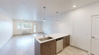 Located in Spokane Valley, WA, this 2-bedroom, 1-bathroom residence offers a well-designed, single-floor layout with a clean, modern aesthetic. The open kitchen and living area serves as the heart of the home, featuring light wood-style luxury vinyl flooring, recessed lighting, and a seamless flow between spaces. The kitchen is outfitted with two-tone cabinetry in a warm wood-grain finish, light countertops, stainless steel appliances including a refrigerator and dishwasher, and ample upper and lower cabinet storage.

The living room is bright and open, with a large window that brings in natural light and offers views of the surrounding greenery. A wall-mounted HVAC unit provides convenient climate control.

Both bedrooms are carpeted and filled with natural light. The primary bedroom is a comfortable size, while the second bedroom features two windows overlooking tree-lined outdoor views. Each room maintains the home's consistent white-wall palette, creating a bright and neutral canvas.

The bathroom is well-appointed with wood-toned vanity cabinetry, a white countertop, a full tub-shower combination, and matching light wood-style flooring. A hallway connects the main living areas to the bedrooms and bathroom, keeping the layout practical and functional throughout.