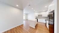 Located at 8440 Phelan Blvd in Beaumont, TX, this single-story residence offers a clean, modern aesthetic across two bedrooms and two bathrooms. The open-concept living and kitchen area is anchored by a central island with a crisp white countertop, complemented by white shaker-style cabinetry, a gray subway tile backsplash, stainless steel sink, and black appliances including a dishwasher, range, microwave, and refrigerator. Warm-toned luxury vinyl plank flooring extends throughout the entire home, creating a cohesive and easy-to-maintain surface. Recessed lighting illuminates the main living area, which flows seamlessly from the kitchen toward a bright living space with natural light from a front-facing window. Both bedrooms are well-proportioned, featuring ceiling fans, large windows with blinds, and access to closet space. The primary bedroom includes a dedicated closet and connects to a sleek en-suite bathroom with a wide vanity, white countertops, large mirror, and a tiled walk-in shower with glass enclosure. The second bathroom mirrors this refined style. Neutral gray walls, clean white trim, and a consistent modern palette give the entire space a fresh, move-in-ready appeal.