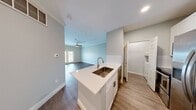 This thoughtfully designed 1-bedroom, 1-bathroom unit offers a comfortable and functional layout across a single floor. The combined kitchen and living area serves as the heart of the home, featuring warm wood-look vinyl plank flooring, crown molding, and ceiling fans that add a classic touch. The kitchen is outfitted with stainless steel appliances — including a side-by-side refrigerator, electric range, and over-the-range microwave — complemented by crisp white shaker-style cabinetry, a subway tile backsplash, and a quartz countertop island with an undermount sink, ideal for both meal preparation and casual dining. The living area benefits from natural light streaming through French doors that open to a private balcony, creating a bright and airy atmosphere. The bedroom is carpeted for comfort, features its own ceiling fan, and is illuminated by a window with outdoor views. The bathroom showcases elegant marble-style tile in the shower surround, adding a refined aesthetic. A dedicated laundry area with stacked washer and dryer hookups is conveniently integrated within the unit. Neutral gray walls and clean white trim throughout lend the space a cohesive, modern feel.