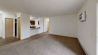 Located at 2700 Hartigan Rd in Volo, IL, this single-floor, one-bedroom, one-bathroom unit offers a functional and comfortable layout. The open-concept combined living and dining area is generously sized, featuring neutral carpet, warm wood-toned baseboards, and a wall-mounted air conditioning unit. A sliding glass door leads directly to a private balcony, filling the space with natural light and providing outdoor access. The galley-style kitchen is efficiently designed with dark cabinetry, dark granite-look countertops, hardwood-style flooring, and black appliances including a refrigerator, range, and dishwasher — all connected to the main living area via a pass-through counter. The bedroom is a comfortable size, carpeted, and features two windows with blinds, a wall-mounted AC unit, baseboard heating, and a walk-in closet with built-in shelving. A versatile den offers additional flexible living or workspace. The full bathroom includes a tiled tub/shower combo with chrome fixtures and built-in shelving niches. Additional highlights include three closets, a dedicated laundry area, an entrance foyer, and a connecting hallway, rounding out a well-organized and practical floor plan.