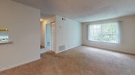 Located at 5820 Murray Dr, Unit H32 in Hanahan, South Carolina, this single-floor residence offers a straightforward and functional layout well-suited for comfortable living. The spacious living area is finished with warm beige carpeting and features a large window dressed with vertical blinds, allowing natural light to fill the room. A textured ceiling and neutral white walls provide a clean, bright backdrop throughout. Adjacent to the living area, a hallway connects the various rooms, including closet storage and access to additional spaces. The kitchen is outfitted with warm-toned oak cabinetry, a double stainless steel sink with a light countertop, tile flooring, and a full-size refrigerator, offering practical utility for everyday use. The unit includes two well-proportioned bedrooms, each featuring plush carpeting, neutral walls, and windows that provide views of the surrounding community. A ceiling fan with integrated lighting is present in one of the rooms, adding to overall comfort. The consistent use of light paint tones and carpet throughout creates a cohesive and inviting atmosphere. The floorplan, as seen in the 3D model, reflects an efficient use of space with clearly defined living, sleeping, and cooking areas all on a single level.