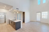 Located at 3100 Martin in Irvine, CA, this thoughtfully designed two-story residence offers a bright, modern living experience across two floors. The main level impresses immediately with soaring double-height ceilings that flood the open-concept kitchen and living area with natural light from tall upper windows. Light wood-tone flooring extends throughout, enhancing the airy atmosphere. The kitchen features a sleek peninsula with a white quartz countertop, dual stainless steel sink, stainless steel appliances including a gas range and microwave, and a two-tone cabinetry scheme of white uppers and dark lower cabinets with pendant lighting. A striking black spiral staircase serves as both a functional and architectural focal point, connecting the main level to the upper loft. The loft area, bathed in recessed lighting, offers a versatile bonus space. The two bedrooms are generously sized, with plush carpeting, ceiling fans, and ample natural light. The primary bedroom is notably spacious and is accompanied by a well-appointed bathroom featuring a double vanity, tub/shower combo, and light wood flooring. Six closets provide abundant storage throughout. A private balcony offers sweeping views of a resort-style pool courtyard, completing this modern Irvine home.