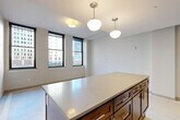 Located at 1249 Griswold St in the heart of downtown Detroit, this one-bedroom, one-bathroom residence offers a well-organized layout across a single floor. The open-concept living, dining, and kitchen area serves as the centerpiece of the home, bathed in natural light from large black-framed windows that frame views of the surrounding cityscape. Pendant globe lighting and flush-mount fixtures illuminate the space with a clean, modern aesthetic.

The kitchen is outfitted with rich dark-wood cabinetry extending to the ceiling, stainless steel appliances including a refrigerator, electric range, and built-in microwave, and a generous island with a light gray quartz countertop that doubles as a dining and prep surface. Tile flooring with a decorative mosaic inlay runs through the kitchen and hallway areas.

A light-filled hallway connects the main living area to the private quarters, lined with three closets offering ample storage, plus a dedicated laundry area. The bedroom features soft carpeting, neutral tones, and a clean, quiet atmosphere. The bathroom is finished with a glass-enclosed shower, tile flooring with mosaic accents, a sleek vanity with an undermount sink, and a mirrored medicine cabinet, delivering a polished and functional design throughout.