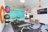 Located at 8400 Veterans Pkwy in Columbus, Georgia, this dynamic fitness facility is thoughtfully designed to serve a wide range of wellness needs under one roof. The space is single-story and organized into several distinct zones, each with its own character and purpose.

The main cardio and strength area is bright and well-lit, featuring an array of treadmills, ellipticals, and cable machines arranged beneath warm orange pendant lighting. Large windows line the walls, allowing generous natural light to fill the space. A dedicated free weights section houses a full rack of dumbbells alongside benches and functional training equipment, including a ceiling-mounted pull-up rig in a bold orange finish.

A separate studio area supports on-demand fitness programming, equipped with a wall-mounted screen, plyo boxes, a rowing machine, and a spin bike — all set against clean white walls and oversized windows. Motivational typography adds energy to the walls throughout.

The children's play room is a colorful highlight, enclosed with glass walls and filled with foam mats, a small slide, gymnastics rings, and soft play structures — keeping younger guests entertained and safe.

A relaxed lounge nook features teal walls, cushioned seating, and a vintage-style arcade table, accented by decorative coastal wall art and cheerful yellow curtains. The entryway is finished with marble-look tile flooring, dual water fountains, and curated artwork, creating a welcoming first impression.