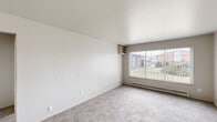 This 2-bedroom, 1-bathroom single-floor unit offers a practical and efficiently organized layout. The living area is carpeted in neutral tones and features a large picture window that fills the space with natural light while providing views of a landscaped outdoor area. A baseboard heating system runs along the perimeter, and a built-in shelf adds a subtle architectural detail to the room.

The kitchen is designed for functionality, featuring gray cabinetry, granite-look countertops, a stainless steel sink, and white appliances including an electric range and full-size refrigerator. Wood-look vinyl flooring and a ceiling fan overhead complete the kitchen's practical aesthetic, which opens toward a small dining area.

The spacious primary bedroom offers generous proportions with soft carpeting, neutral walls, and a closet, while the second bedroom is similarly finished with carpet, a window with vertical blinds, and a built-in shelf nook. A hallway connects the main rooms to the full bathroom, which includes a soaking tub, toilet, wood-look vinyl flooring, and open shelving. A dedicated closet provides additional storage within the unit.