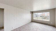 This 2-bedroom, 1-bathroom single-floor unit offers a practical and efficiently organized layout. The living area is carpeted in neutral tones and features a large picture window that fills the space with natural light while providing views of a landscaped outdoor area. A baseboard heating system runs along the perimeter, and a built-in shelf adds a subtle architectural detail to the room.

The kitchen is designed for functionality, featuring gray cabinetry, granite-look countertops, a stainless steel sink, and white appliances including an electric range and full-size refrigerator. Wood-look vinyl flooring and a ceiling fan overhead complete the kitchen's practical aesthetic, which opens toward a small dining area.

The spacious primary bedroom offers generous proportions with soft carpeting, neutral walls, and a closet, while the second bedroom is similarly finished with carpet, a window with vertical blinds, and a built-in shelf nook. A hallway connects the main rooms to the full bathroom, which includes a soaking tub, toilet, wood-look vinyl flooring, and open shelving. A dedicated closet provides additional storage within the unit.