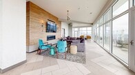 Located at 120 Piedmont Ave NE in downtown Atlanta, this high-rise amenity lounge offers a sophisticated and open communal space designed for both relaxation and social gatherings. The single-floor layout is defined by dramatic floor-to-ceiling curtain-wall windows that wrap around much of the perimeter, flooding the interior with natural light and providing sweeping panoramic views of the Atlanta skyline. Large glass doors open directly onto an outdoor terrace, extending the usable space and offering an al fresco setting with additional seating overlooking the cityscape.

The interior is finished with light-toned herringbone-patterned tile flooring throughout, lending a clean and modern aesthetic. A warm lounge area anchors one end of the space, featuring a linear gas fireplace set into a wood-paneled accent wall with wall sconces and a wall-mounted television above — ideal for casual gatherings. Plush seating, including a sectional sofa and accent chairs in teal and cognac leather with brass-finished frames, adds color and comfort.

A dining area with a large marble-topped table and an eclectic mix of bistro-style chairs provides a functional space for communal dining or meetings. Structural columns are finished in a textured material, complementing the contemporary design. The overall ambiance is bright, airy, and upscale, making this an exceptional shared amenity space in the heart of Atlanta.