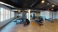 Located at 29–69 First Ave NW in Hickory, NC, this single-floor fitness facility offers a spacious and thoughtfully organized workout environment. The space features a striking industrial aesthetic, defined by a dramatic exposed ceiling with dark-painted structural beams, ductwork, and pendant lighting that creates a modern, warehouse-inspired atmosphere.

The flooring throughout is a warm hardwood-style material that provides both durability and visual appeal. The facility is divided into distinct functional zones. The cardio area is lined with treadmills, stationary bikes, and elliptical machines, complemented by wall-mounted flat-screen televisions. A dedicated strength training section houses a multi-station functional trainer, a dumbbell rack with a full range of weights, medicine balls, and a mini trampoline for dynamic training. Full-length mirrors are positioned along multiple walls, enhancing the sense of space and supporting proper form during workouts.

A separate, open flex area with clean white walls and light flooring offers versatile space suitable for stretching, group classes, or mat-based training. Natural light filters in through windows along one wall, brightening the main workout floor. Additional amenities include a water fountain station and clearly marked exits. The overall ambiance is energetic yet clean, making this facility well-suited for a wide range of fitness activities.
