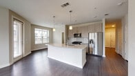 This two-bedroom, two-bathroom unit in Lawrenceville, Georgia is laid out on a single floor and offers a well-designed open-concept living space. The kitchen serves as a central focal point, featuring a large island with granite countertops and an undermount sink, light wood-toned cabinetry extending to the ceiling, a subway tile backsplash, and a full suite of stainless steel appliances including a gas range, microwave, and French door refrigerator. Pendant lighting above the island adds a modern touch. The kitchen flows directly into the living and dining area, which is finished with dark hardwood-style flooring, neutral-toned walls, and a ceiling fan. Multiple windows along the perimeter allow natural light to fill the space and provide outdoor views.

A hallway connects the common areas to the two bedrooms, each carpeted and equipped with a ceiling fan and window. Both bedrooms offer access to their own full bathrooms, each finished with granite-topped vanities, tile flooring, and a tub-shower combination with tile surround. The primary bedroom also includes a dedicated walk-in closet. The overall aesthetic is clean and contemporary throughout.