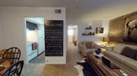 This single-floor residence blends rustic charm with modern sensibility through a carefully curated interior design. The living room serves as the standout space, anchored by a full exposed brick accent wall that lends warmth and texture to the room. Cream upholstered sofas, a reclaimed wood coffee table, and a cowhide rug ground the space, while a large equestrian-themed artwork displayed against the brick wall adds a bold focal point. Floating wooden shelves and ambient lamp lighting complete the inviting atmosphere.

Adjacent to the living area, the dining space accommodates a round wooden table with wrought iron chairs, accented by decorative wall art. A large Houston street-sign artwork marks the transition toward the kitchen, which features white appliances including a refrigerator and range, with hard flooring for easy maintenance.

The bedroom offers carpeted flooring, a window with floor-length drape panels allowing natural light, and dual closet doors providing generous storage. A rustic wooden dresser and decorative accents contribute to the cohesive aesthetic carried throughout the residence.

The bathroom includes a tub-shower combination finished with classic white square tile and a patterned shower curtain. Overall, the space presents a consistent rustic-modern character with thoughtful detailing throughout.