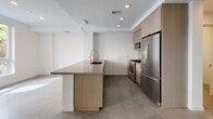 Located at 222 W Sixth St in the San Pedro neighborhood of Los Angeles, this two-story space presents a clean, contemporary aesthetic defined by polished concrete floors, crisp white walls, and an open, light-filled layout throughout both levels.

The main living area is anchored by an open-plan kitchen featuring warm wood-tone cabinetry that extends to the ceiling, a stone-topped peninsula with an integrated sink, and a full suite of stainless steel appliances including a gas range, microwave, and French door refrigerator. Recessed and linear lighting highlights the kitchen's refined finishes. The adjacent living area benefits from large windows that invite natural light and urban views of the surrounding San Pedro streetscape.

The bedrooms are generously proportioned, each offering polished concrete flooring and large windows framing neighborhood views. Multiple bathrooms serve the residence, including a primary bath with a lengthy double-vanity, warm wood cabinetry, backlit mirrors, and a walk-in closet. A secondary bath features a combined tub and shower with white tile surround, while a half bath provides a single vanity with neutral stone countertop. The overall ambiance is minimal, modern, and functional throughout both floors.