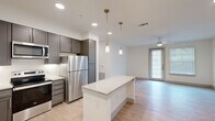 This thoughtfully designed 1-bedroom, 1-bathroom unit offers a cohesive and modern living experience across a single floor. The open-concept kitchen and living area serves as the heart of the unit, where a granite-topped center island anchors the space and provides additional prep and seating options. The kitchen features gray shaker-style cabinetry, stainless steel appliances including a refrigerator and dishwasher, a classic white subway tile backsplash, and light hardwood-style flooring that flows seamlessly into the living area. Pendant lighting above the island and recessed ceiling lights add a layered, well-lit ambiance throughout. The living room is bright and airy, highlighted by a ceiling fan, large windows with blinds, and a glass door that invites natural light and outdoor access. The bedroom is a comfortable retreat with plush carpeting, a ceiling fan, natural light from a window, and access to closet storage. The bathroom is clean and functional, finished with large-format tile flooring, a vanity with stone countertop, and crisp white walls. Two closets provide ample storage throughout the unit, and a hallway connects the spaces efficiently for a practical and comfortable daily flow.