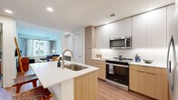 Located on Fourth Ave N in Nashville's downtown core, this single-story, one-bedroom, one-bathroom unit offers a thoughtfully designed layout across a compact but efficient floor plan. The interior features consistent light wood-style flooring throughout, recessed lighting, and a clean, modern aesthetic defined by white walls and warm natural wood tones.

The kitchen serves as a central feature of the unit, anchored by a peninsula with a white quartz countertop and undermount stainless steel sink. Cabinetry combines white upper cabinets with natural wood lower cabinets, providing ample storage. Stainless steel appliances include a French door refrigerator, range with microwave above, and dishwasher integrated into the peninsula. A subway tile backsplash adds a refined finishing detail.

The living room benefits from natural light through large windows dressed with sheer drapes, creating a welcoming, airy atmosphere. Open shelving in the hallway provides additional storage and display space near the entryway.

The bedroom features a generous window mirroring the living area's natural light and offers comfortable accommodation. The bathroom is well-appointed with a glass-enclosed walk-in shower, a wood-toned vanity with white countertop, and a backlit mirror. A dedicated in-unit stacked washer and dryer is conveniently accessible from the bathroom area.