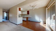 This single-floor unit is designed with a practical, open layout that connects the kitchen and living areas seamlessly. The kitchen is equipped with white appliances, including a range and refrigerator, complemented by a mix of wood-toned and white cabinetry offering generous storage. Open shelving adds a functional display element, while a built-in breakfast bar provides additional counter space and a casual dining option. Hardwood flooring runs throughout the kitchen, adding warmth and durability to the space.

The living area is expansive and carpeted, bathed in natural light from a sliding glass door that opens to an outdoor balcony with views of surrounding greenery. A ceiling fan with a light fixture provides both ventilation and overhead lighting. A wall-mounted air conditioning unit and baseboard heating ensure year-round climate comfort.

The bedroom is a well-proportioned, carpeted room featuring a large sliding window that frames outdoor views and admits ample natural light. A ceiling fan adds comfort to this restful space. The full bathroom is finished with classic white square tile lining the tub surround and walls, complemented by tile flooring, a built-in tub with an overhead shower, and a vanity with wood cabinetry.