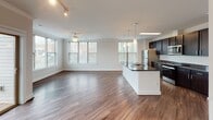 Located at 2150 Bond St. in Charlottesville, Virginia, this single-floor residence offers a thoughtfully designed layout with modern finishes and a cohesive aesthetic throughout. The open-concept kitchen and living area serves as the heart of the home, featuring rich dark cabinetry, granite countertops, stainless steel appliances including a built-in microwave, electric range, and refrigerator, all complemented by warm wood-tone flooring. Pendant lighting over the kitchen island and track lighting in the living area add functional style to the space. A long, well-lit hallway connects the main living area to the private rooms, lined with crisp white panel doors and crown molding that lend a clean, polished look. The bedrooms are carpeted for comfort and feature large windows that invite generous natural light and views of the surrounding greenery and neighborhood. The bathrooms are finished in bright white tile, with one offering a soaking tub and shower combination and another featuring a dedicated walk-in shower. The overall ambiance of the residence is modern and move-in ready, with a neutral color palette and quality finishes that provide a versatile backdrop for any style of living.