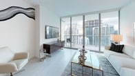 This contemporary high-rise residence at 49L offers a refined, single-floor layout defined by clean lines, a neutral palette, and an abundance of natural light. The open-concept living and dining area is anchored by expansive floor-to-ceiling windows that frame striking panoramic city skyline views, seamlessly connecting the interior to a private balcony. Light-toned wood flooring flows throughout, contributing to the bright and airy atmosphere.

The kitchen is outfitted with high-gloss white cabinetry, dark countertops, and a full suite of stainless steel Bosch appliances, including a built-in oven, microwave, induction cooktop, and dishwasher. A breakfast bar with white modern barstools provides a casual dining option, while a built-in wine cooler adds an upscale touch to the entertaining area.

The primary bedroom enjoys direct access to the city views through floor-to-ceiling glazing and is complemented by a spa-inspired en-suite bathroom featuring marble tile flooring, a double vanity with white cabinetry, and a walk-in closet. An additional lounge or flex room offers a versatile space with a comfortable sofa. A minimalist powder room with contemporary fixtures and curated wall art completes this well-appointed residence.